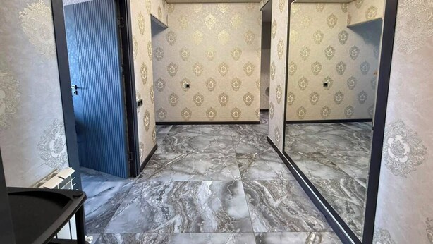 Un pasillo con papel tapiz estampado, suelo de mármol y un espejo grande.