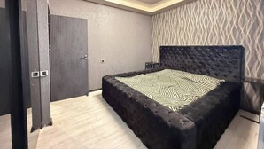 Un dormitorio con una cama grande, cabecera oscura y pared con estampado.