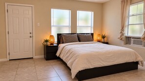 A bedroom with a bed, two bedside tables, a door, and windows with blinds. - Pet-Friendly Home w/ Patio & Backyard (Houston)