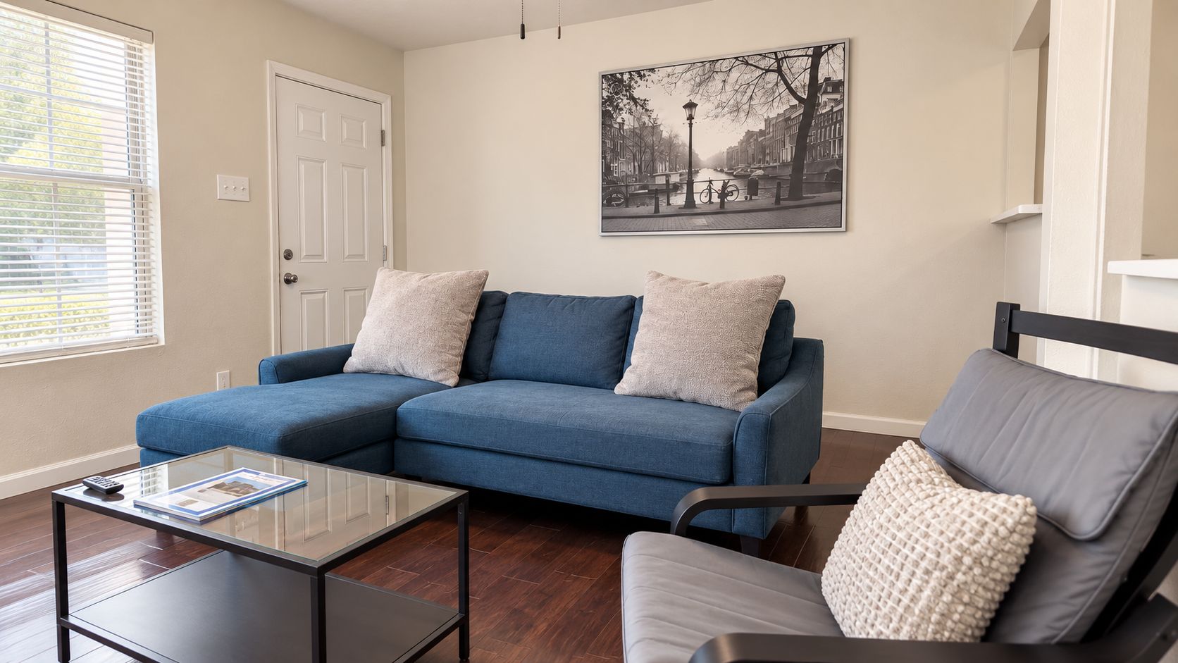Ein Wohnzimmer mit einem blauen Ecksofa, einem Glastisch und einem grauen Sessel.