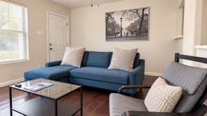 A living room with a blue sectional sofa, a glass coffee table, and a gray armchair. - Pet-Friendly Home w/ Patio & Backyard (Houston)