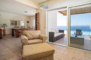 Un salon comprenant un canapé, un pouf, un coin repas et une porte-fenêtre coulissante donnant sur un balcon avec vue sur la mer.