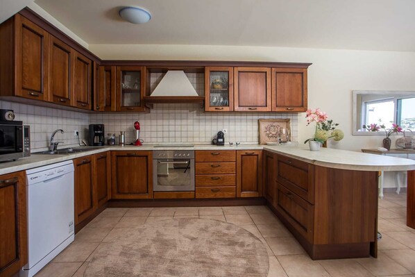 A kitchen with wooden cabinets, a dishwasher, a stove, and a microwave. - Miranda Infinity Pool Villa Pefkos Rhodes (Rhodes)