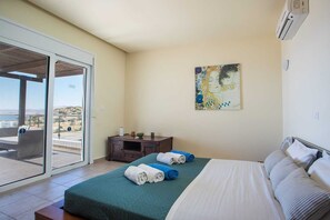 A hotel room with a bed, a painting, a desk, and a view through a glass door. - Miranda Infinity Pool Villa Pefkos Rhodes (Rhodes)