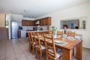 A modern kitchen with wooden cabinets, a built-in oven, and a dining area with a wooden table and chairs. - Miranda Infinity Pool Villa Pefkos Rhodes (Rhodes)