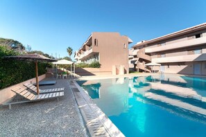 A swimming pool with lounge chairs and umbrellas, surrounded by buildings with balconies. - Golden Sun Adults-Only Luxury Apartment in Rhodes (Rhodes)