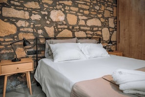 A bed with white bedding, a nightstand with a lamp, and a stone wall. - Manolis Seaside Villa with Private Pool, 500m from the Beach (Rhodes)