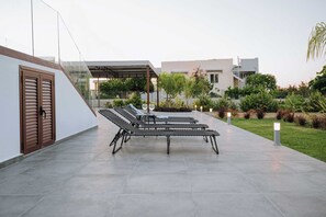 A modern outdoor seating area with lounge chairs and tables, a covered patio, and a well-maintained garden. - Manolis Seaside Villa with Private Pool, 500m from the Beach (Rhodes)