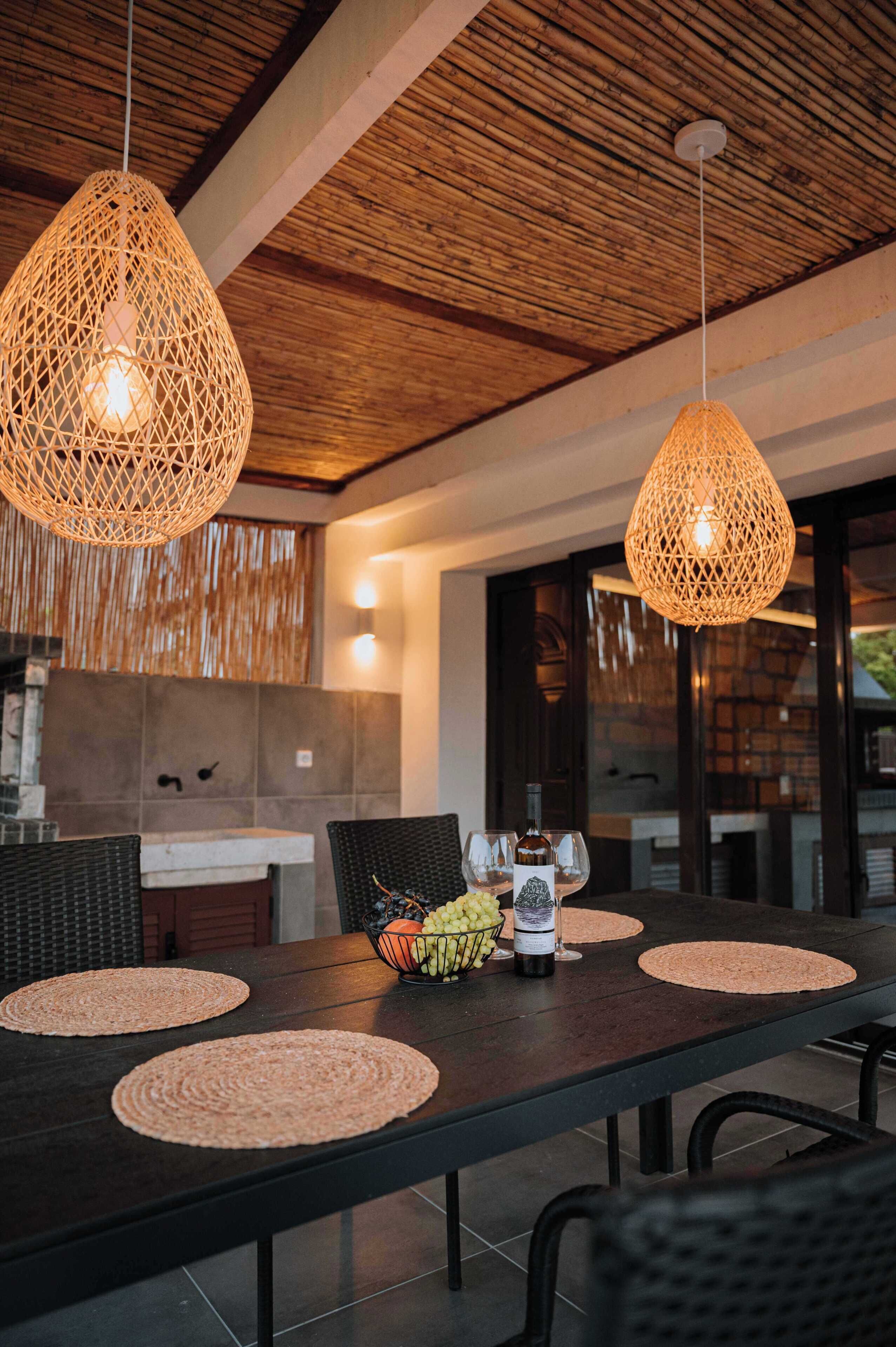 A dining area with a long table, woven pendant lights, and a bottle of wine.