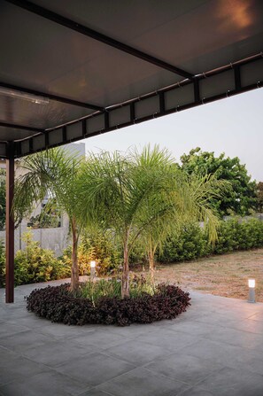 A covered outdoor area with a concrete floor, surrounded by various plants and trees. - Manolis Seaside Villa with Private Pool, 500m from the Beach (Rhodes)