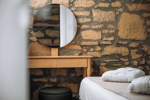 A room with a stone wall, a round mirror, a wooden bedside table, and a bed with a white blanket. - Manolis Seaside Villa with Private Pool, 500m from the Beach (Rhodes)
