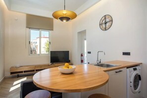 A modern kitchen with a round wooden table, a washing machine, and a built-in TV. - 2BR Apartment with 2 Bathrooms in Rhodes Center (Rhodes)