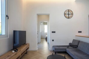A modern living room with a flat-screen TV on a wooden stand, a grey sofa, and a wall-mounted clock. - 2BR Apartment with 2 Bathrooms in Rhodes Center (Rhodes)