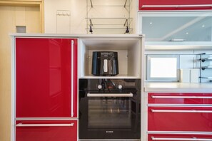 A kitchen with red cabinetry, a Bosch oven, and a coffee maker. - Crethion | Private Pool, Jacuzzi, Gym & Games Room (Violi Charaki)