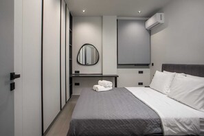A modern hotel room with a bed, a bedside table with towels, a mirror, and an air conditioning unit. - Kennedy 16 Urban Escape Rhodes Town, Apartment (Rhodes)