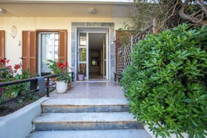 A building entrance with steps leading up to a door, a potted plant, and a small garden area with a hedge. - Kennedy 16 Urban Escape Rhodes Town, Apartment (Rhodes)