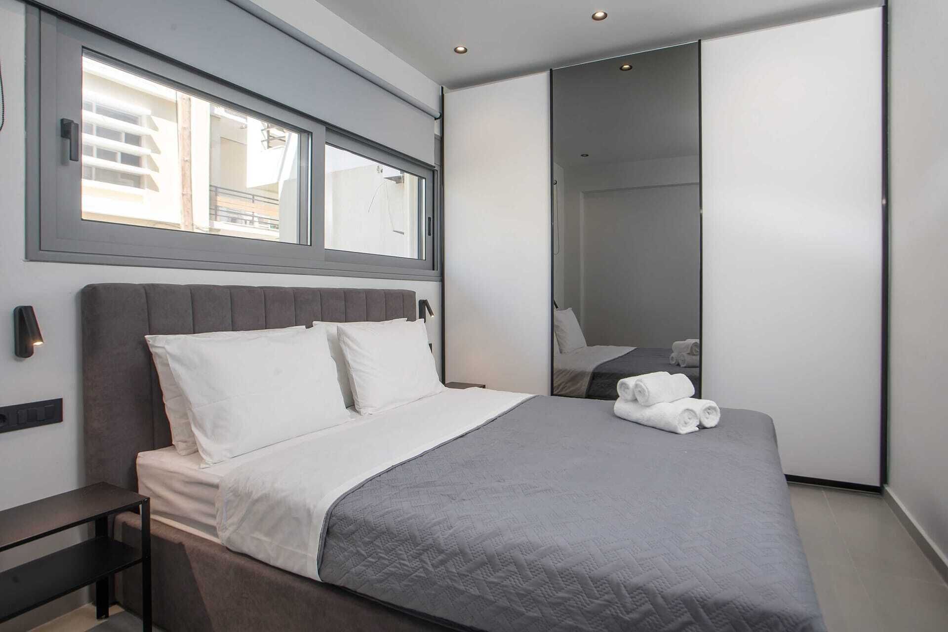 Ein modernes Schlafzimmer mit einem Bett, einem Nachttisch, einem Fenster und einem Spiegel.