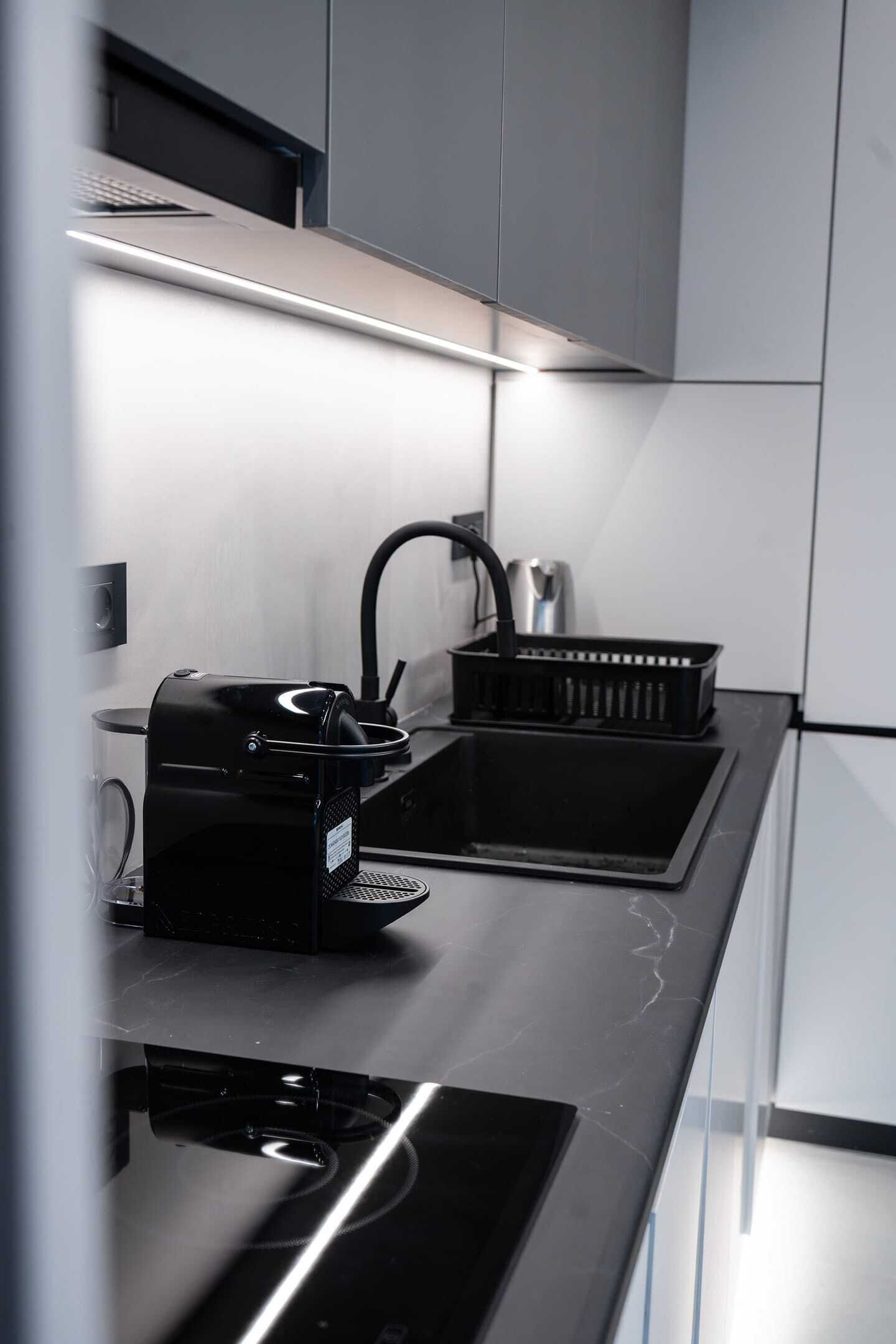 Una cocina moderna con cafetera integrada, un lavamanos y una jarra de café negra.