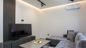 Ett modernt vardagsrum med en platt-TV, en grå soffa och ett soffbord med frukt på.