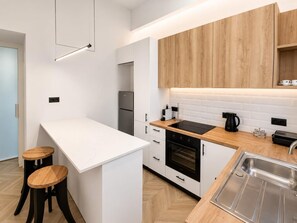 A modern kitchen with white cabinetry, a wooden countertop, a built-in oven, a sink, and two stools. - Mandilara City Hideaway – Adults Only (Rhodes)