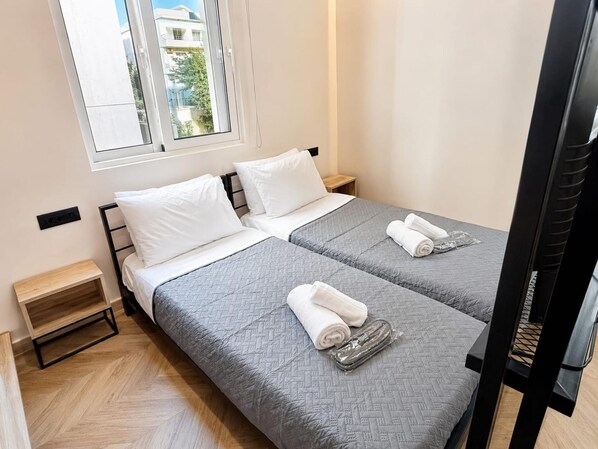 A double bed with grey bedding and white pillows, a wooden nightstand, and a window with a view of buildings. - Mandilara City Hideaway – Adults Only (Rhodes)