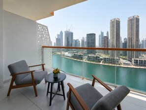 A balcony with two grey armchairs, a small round table with a vase, and a city view overlooking a body of water and high-rise buildings. - Panoramic Burj Khalifa and Canal View, Business Bay, Dubai, UAE (Dubai)