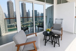 Ein moderner Balkon mit Stadtblick, zwei graue Sessel, ein kleiner runder Tisch und eine Vase mit Blumen.