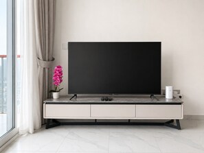 Una sala moderna con un televisor de pantalla plana grande sobre un mueble minimalista, una orquídea en maceta y una cafetera en la encimera.