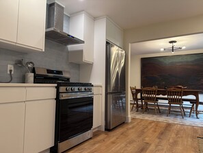 A modern kitchen with stainless steel appliances, white cabinetry, and a dining area with wooden chairs. - Bucks Lodge - Heart of the Catskills (Elka Park)
