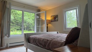 Un dormitorio con cama, escritorio, ventilador de techo y ventanas amplias con cortinas.