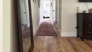 Un pasillo con piso de madera, un espejo grande, un televisor de pantalla plana montado en la pared y una puerta que da a otra habitación.