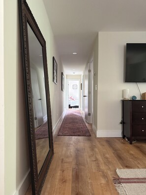 Ein Flur mit Holzboden, einem großen Spiegel, einem an der Wand befestigten Flachbildfernseher und einer Tür zu einem weiteren Zimmer.