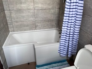 A bathroom with a bathtub, a shower curtain, and a toilet.