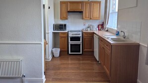 A compact kitchen with wooden cabinets, a microwave, a stove, and a sink. - Coastal Place (Scarborough)
