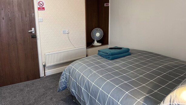 A hotel room with a bed, a TV mounted on the wall, a fan, and a 'No Smoking' sign. - Coastal Place (Scarborough)
