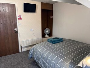 A hotel room with a bed, a TV mounted on the wall, a fan, and a 'No Smoking' sign. - Coastal Place (Scarborough)
