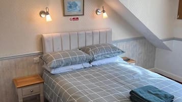 Un dormitorio con cama, dos mesitas de noche, lámpara de pared e imagen enmarcada.