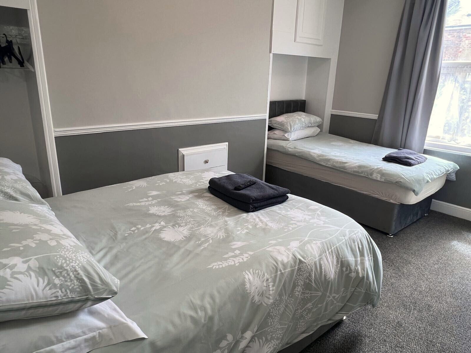 A room with a large bed, a smaller bed, a nightstand, and a window with curtains.