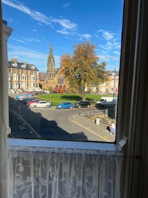 A view from a window overlooking a street with parked cars, a church with a tall spire, and a tree with autumn leaves. - Coastal Place (Scarborough)