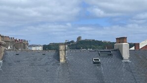 A rooftop with a view of a historic castle, a chimney, and a clear sky. - Coastal Place (Scarborough)