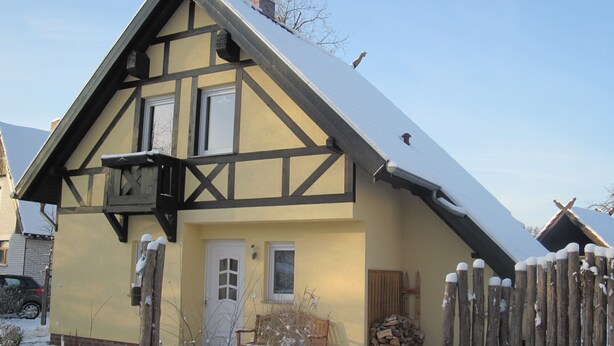 Une maison traditionnelle à colombages, avec un toit enneigé, une clôture en bois et une pile de bois de chauffage.