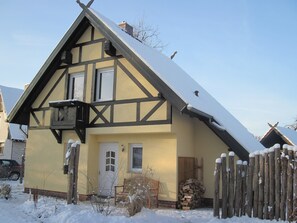 A traditional half-timbered house with a snow-covered roof, a wooden fence, and a stack of firewood. - Romantic vacation home nestled in the heart of the Spreewald countryside—pure tranquility (Burg (Spreewald))