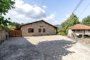 A stone building with a tiled roof, a paved driveway, and a wooden fence.