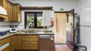 Cocina con armarios de madera, pileta de acero inoxidable, lavavajillas integrado y ventana con vista a follaje.