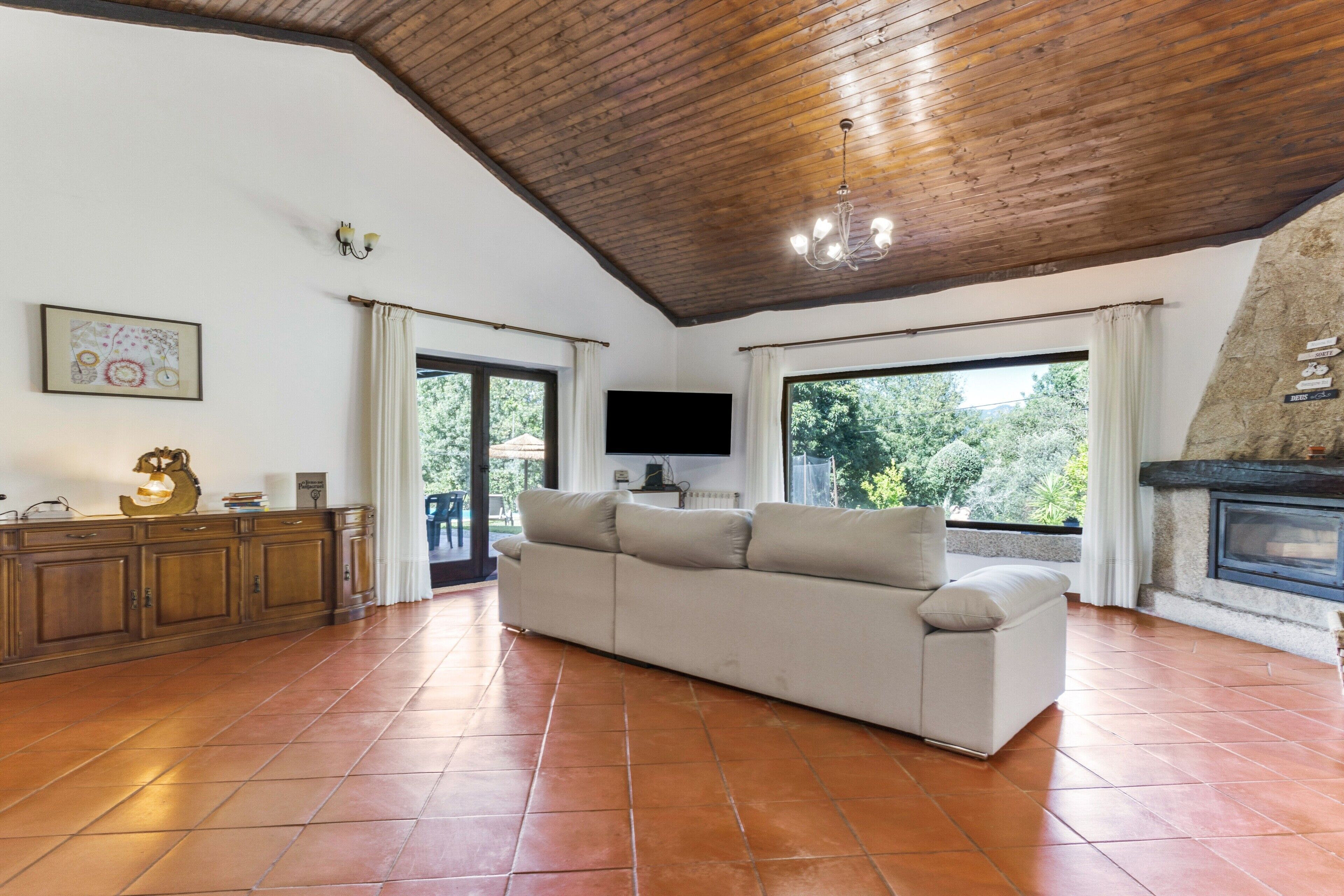 A spacious living room with a high ceiling, a fireplace, a large window, and a television.
