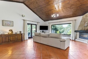A spacious living room with a high ceiling, a fireplace, a large window, and a television.