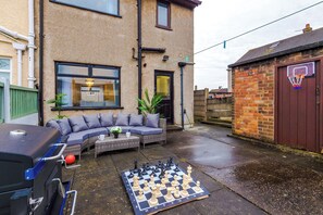An outdoor seating area with a sofa, a chessboard, and a barbecue grill. - Long Stays | 2 Bed | St Helens | Sleeps 5 (St Helens)