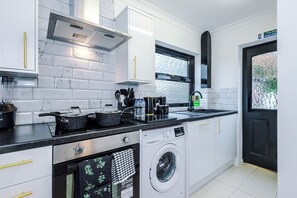 A modern kitchen with white cabinets, a black countertop, a built-in oven, a dishwasher, and a washing machine. - Long Stays | 2 Bed | St Helens | Sleeps 5 (St Helens)