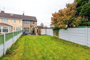 A residential backyard with a lawn, a white fence, and a house with a conservatory. - Long Stays | 2 Bed | St Helens | Sleeps 5 (St Helens)