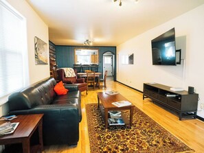 A living room with a sofa, coffee table, and TV. There is a dining area with chairs and a table in the background. - Wolf Creek FishHouse (Wolf Creek)